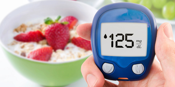 Hand hält ein blaues Blutzuckermessgerät mit Anzeige 125 mg/dL, im Hintergrund eine grüne Schüssel mit Müsli und Erdbeeren.